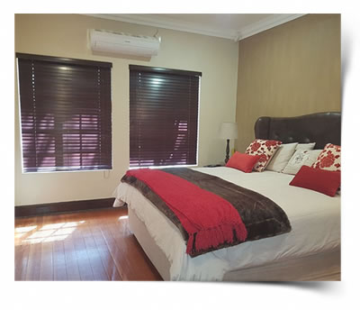Two Basswood dark mahogany colour blinds blends in with bedding and wooden flooring of this bedroom in Bayswater Bloemfontein.