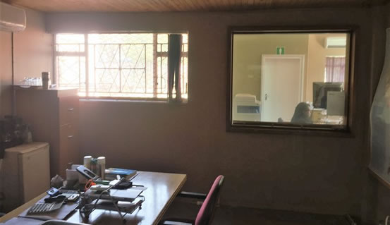 The image shows the old Vertical blinds still on the window before our installation of Venetian Blinds. The sun catches the window directly and fills the room with light.